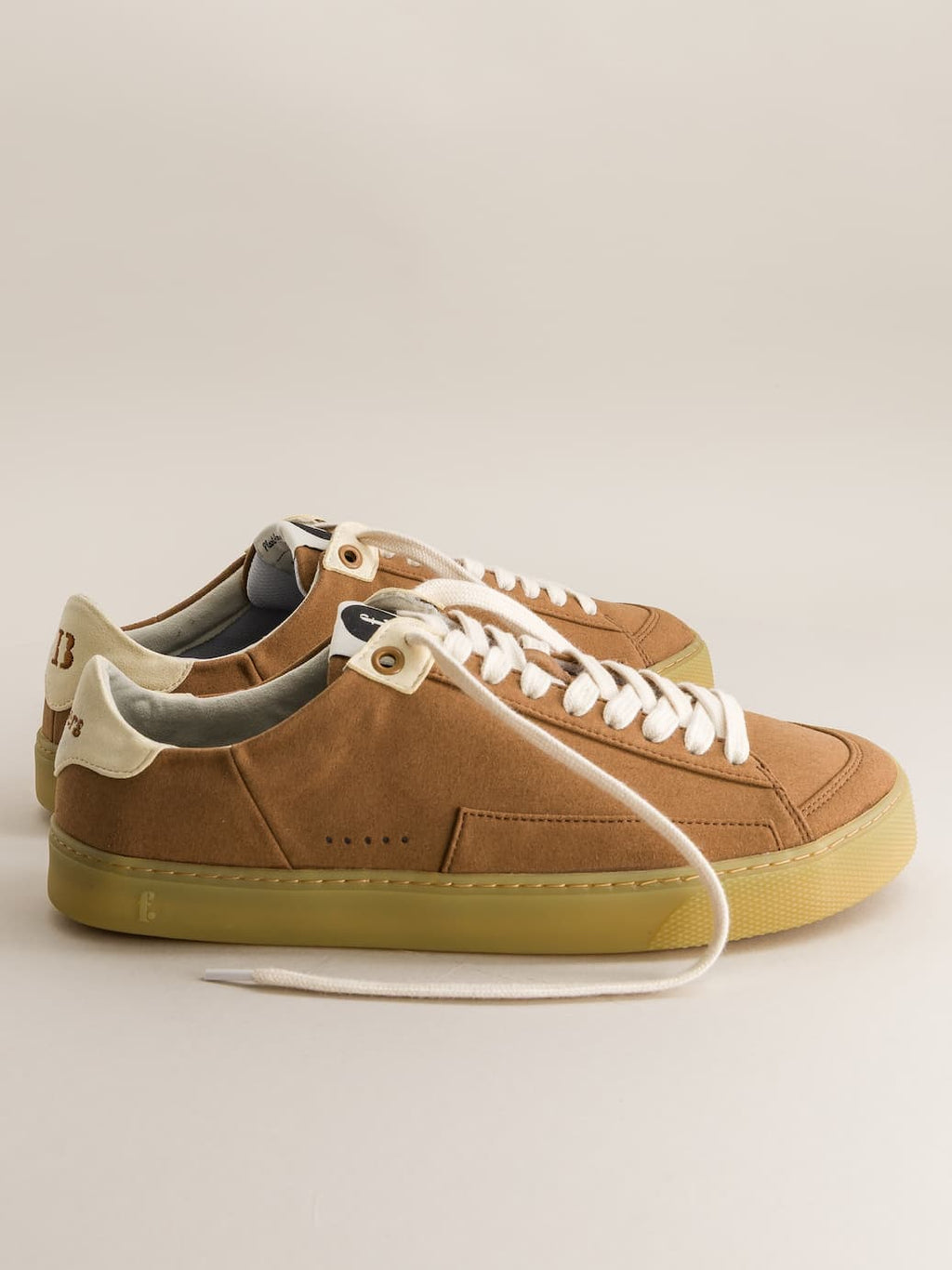 Brown barefoot sneakers with white laces on a beige background