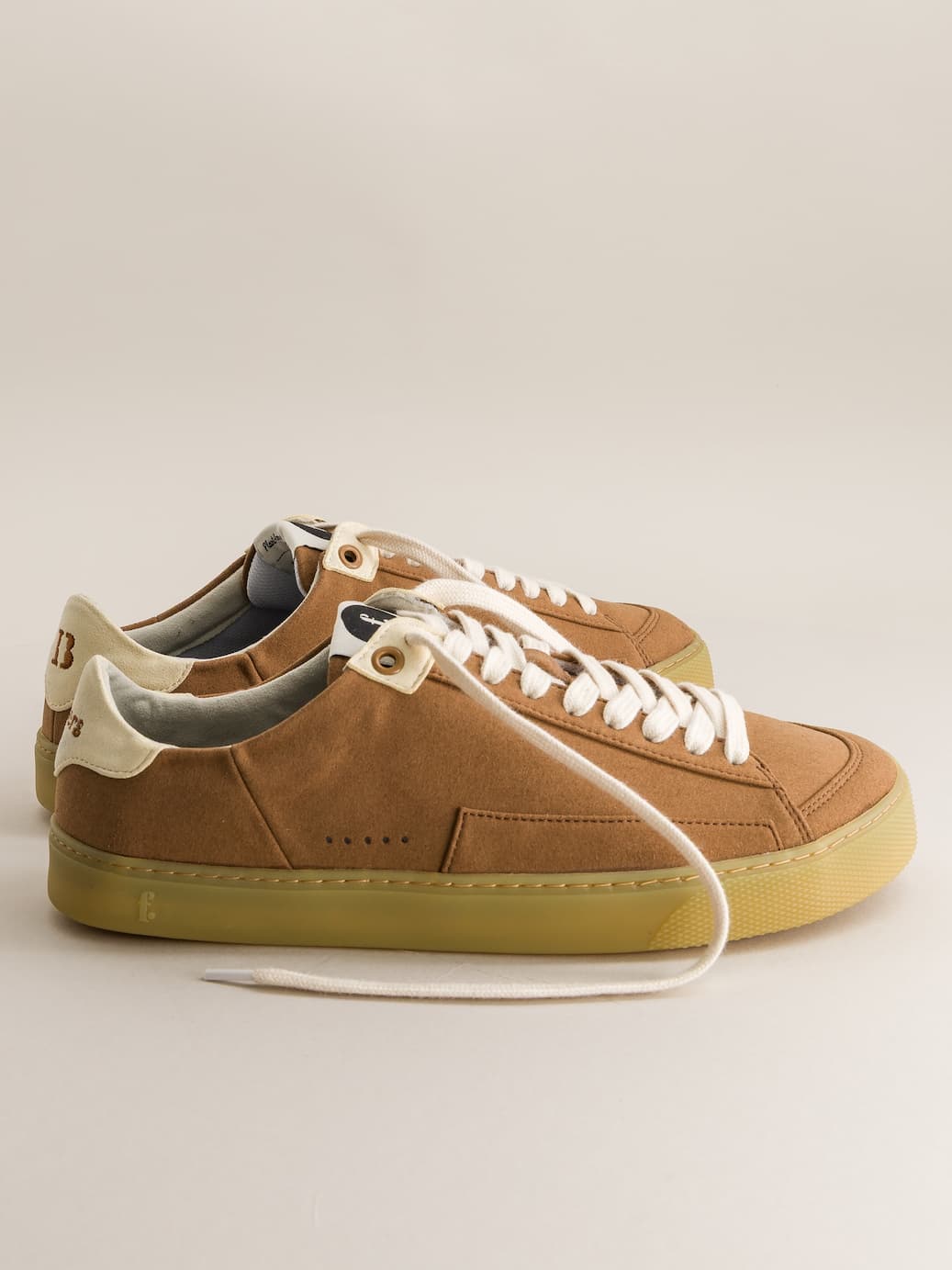 Brown barefoot sneakers with white laces on a beige background