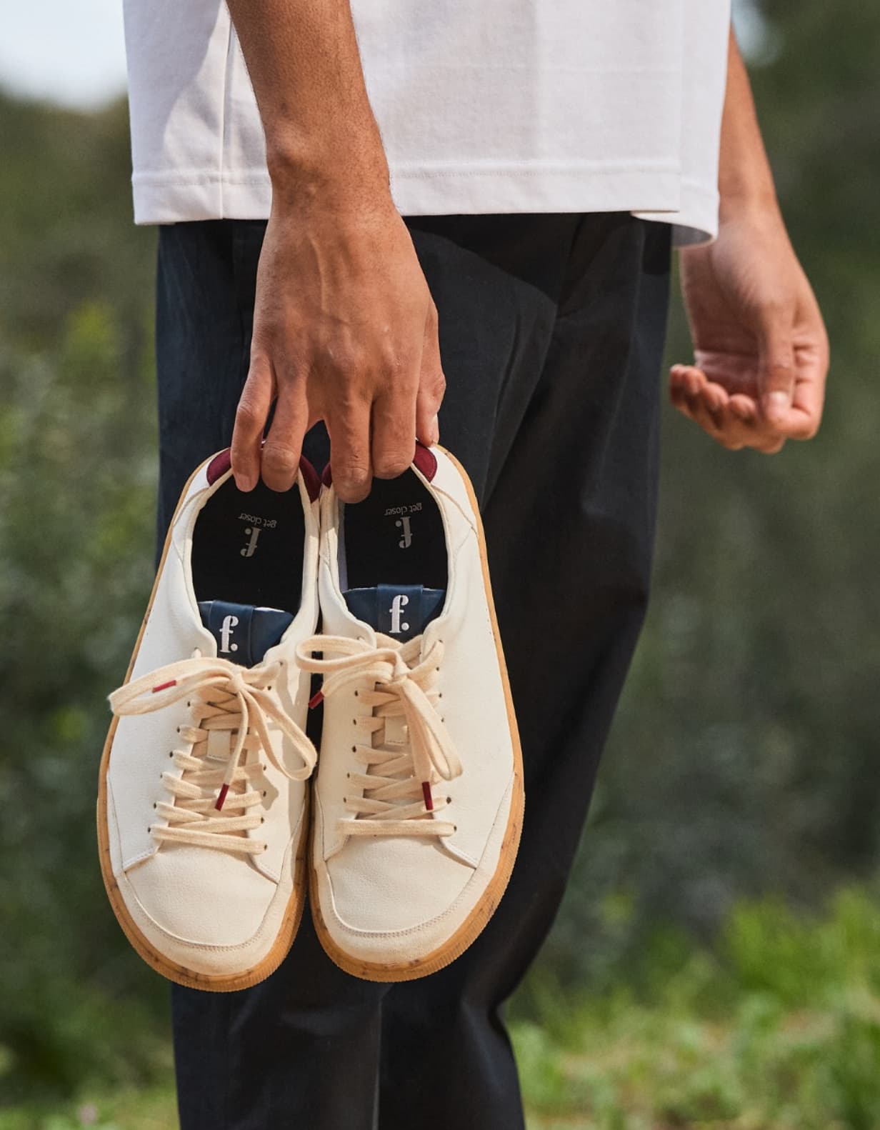 Person holding a pair of white barefoot sneakers with a blurred natural background